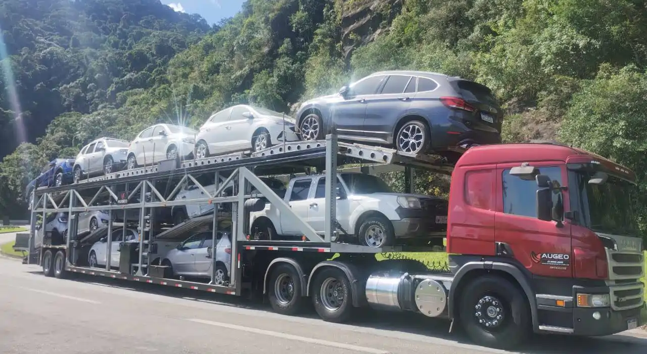 Caminhão cegonha transportando vários carros em rodovia, representando operação de transporte automotivo com veículo de linha pesada.